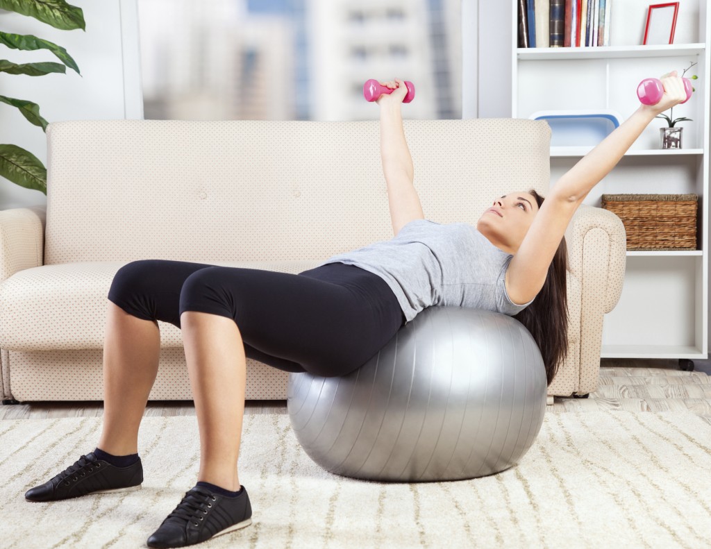 Picture of a girl working out in living room with an exercise ball.